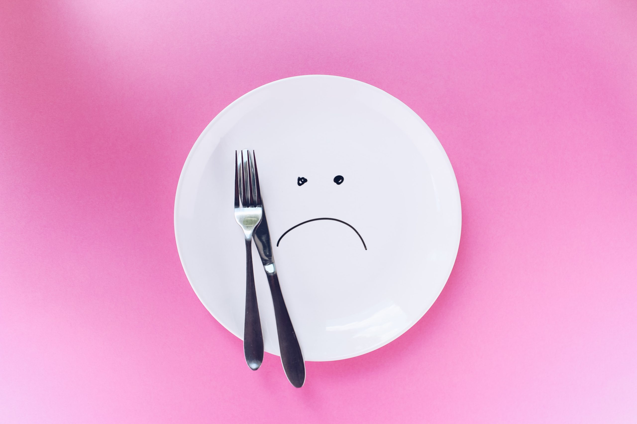 why diets always fail sad face written on an empty white plate on pink background